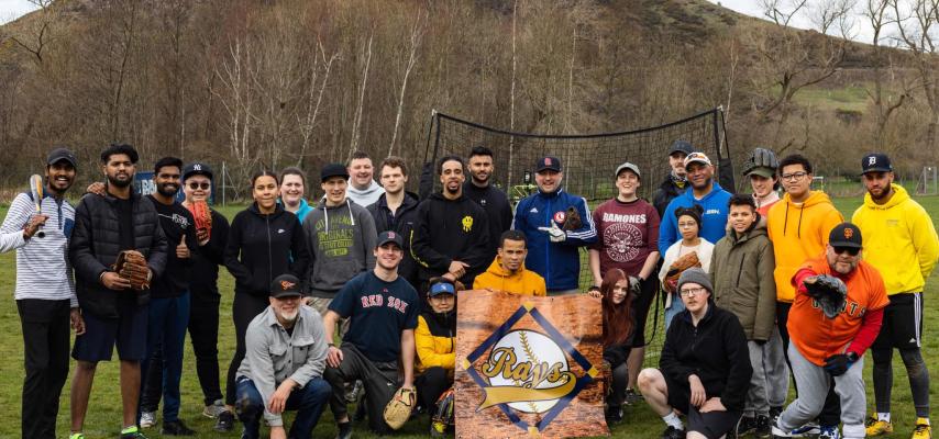 Group shot of the Edinburgh Rays baseball in playing field, standing/crouching around their logo