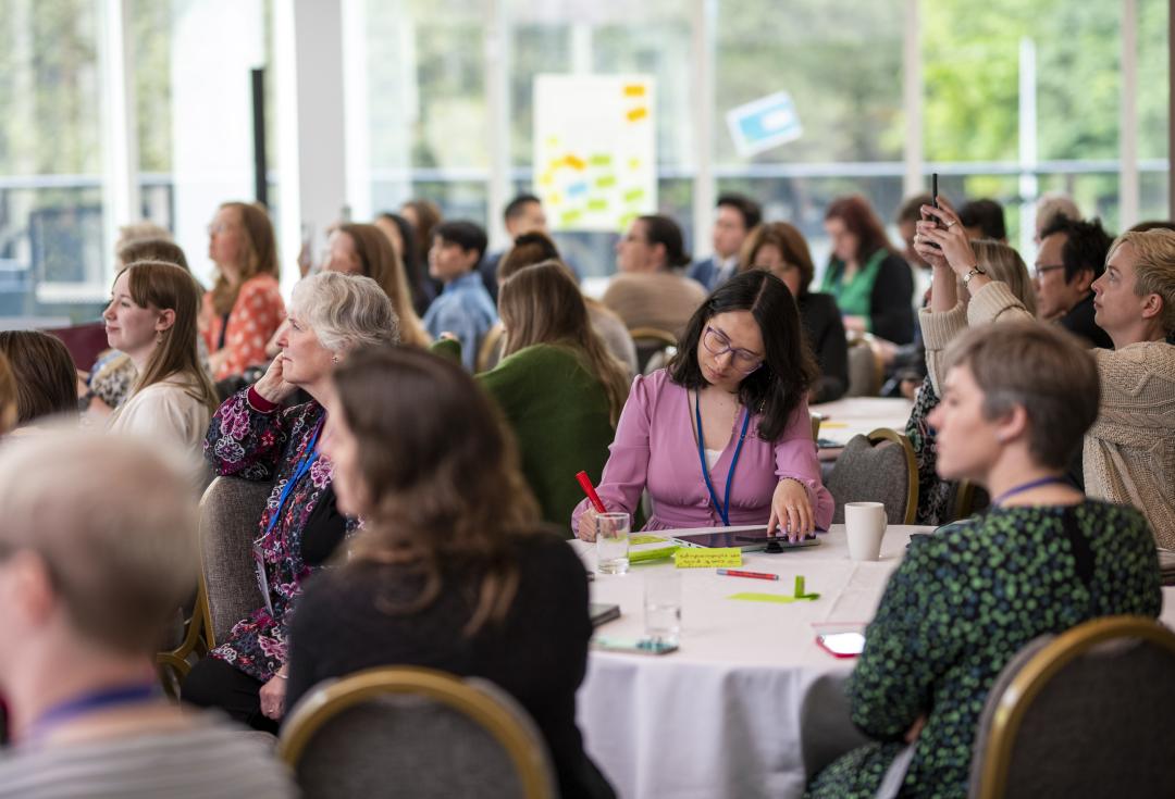 A group of people at Engage conference sitting around tables listening at a panel session