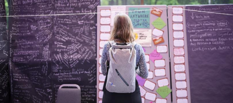 A woman stands in front of a board covered in post-it notes